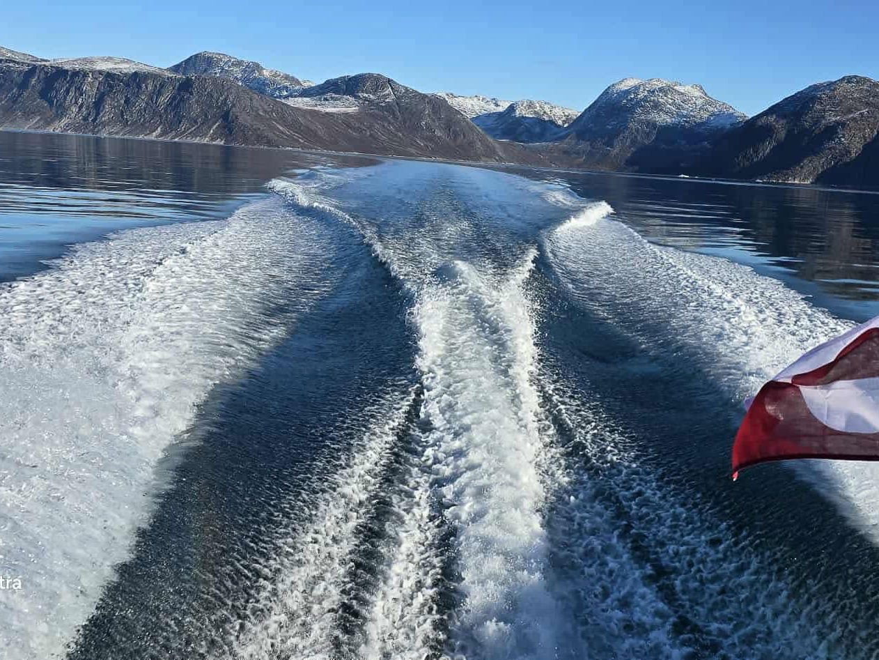 Skumsprøjt agter på båd, der sejler langs de grønlandsk bjerge